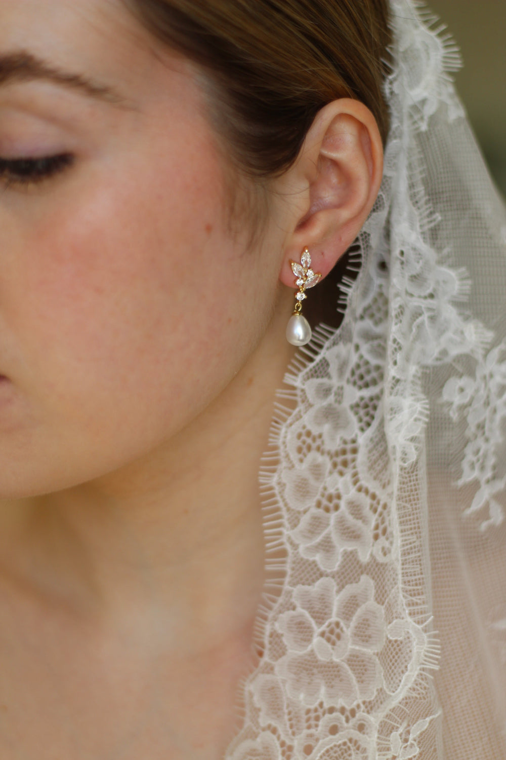 Close-up of a person wearing a delicate pearl earring with a lace veil in the background