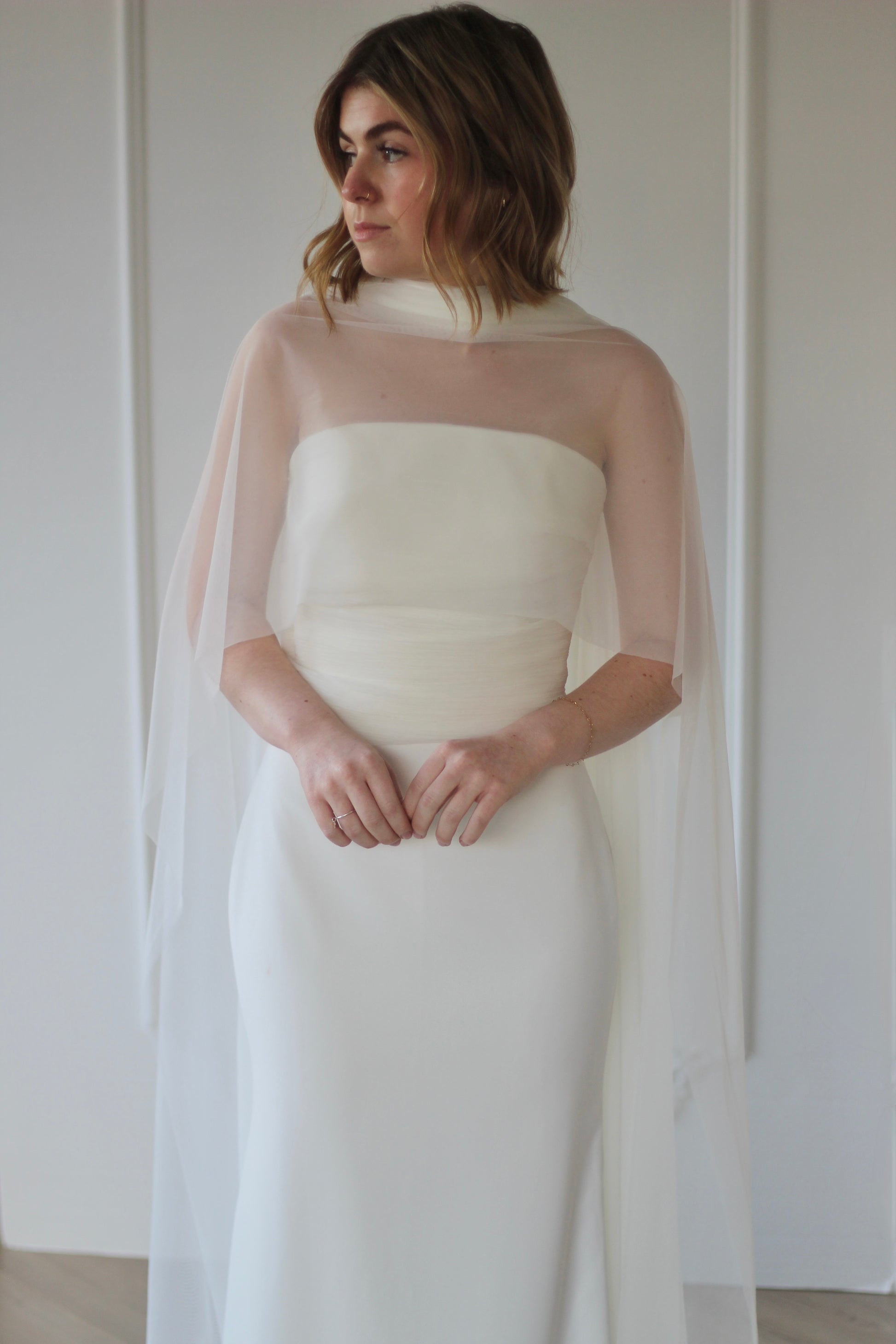 Woman wearing a white wedding dress with a sheer overlay against a plain background
